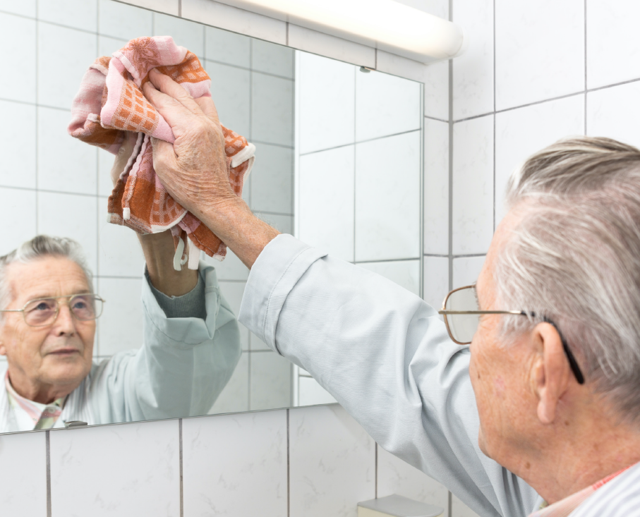 Ældre mand tørrer et spejl af med en klud. Man kan se hans ansigt i spejlet.